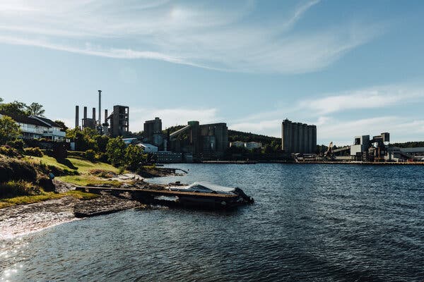 A large factory building near the shore of a body of water.