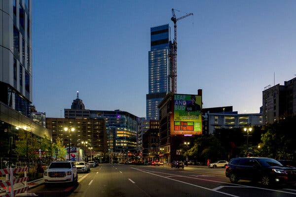 A skyscraper with buildings around it and a construction crane, seen at the end of a street, at night.