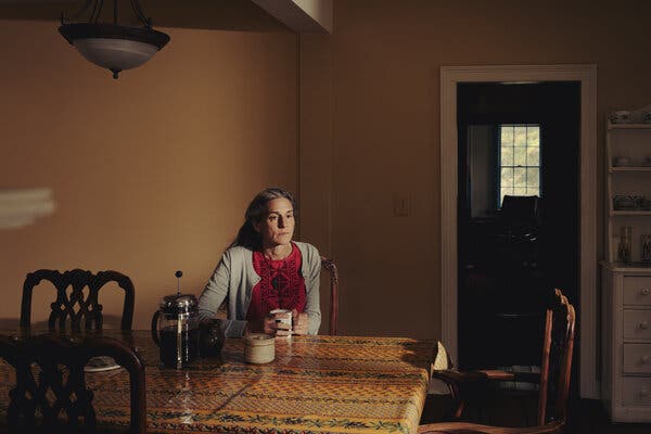 Nadia Milleron is seated at a table in a kitchen wearing a red shirt and light cardigan, holding a white mug.