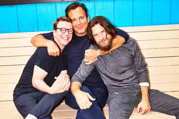 Sean Hayes, Will Arnett and Jason Bateman sitting on a wooden bench with their arms around one another.