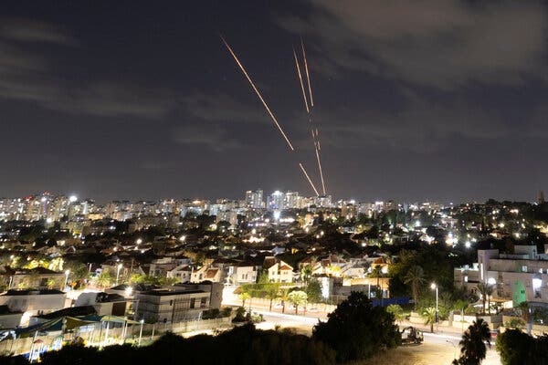 Three streaks of light cross the sky above the skyline of Ashkelon, Israel, as Israel’s antimissile system intercepts projectiles from Iran.