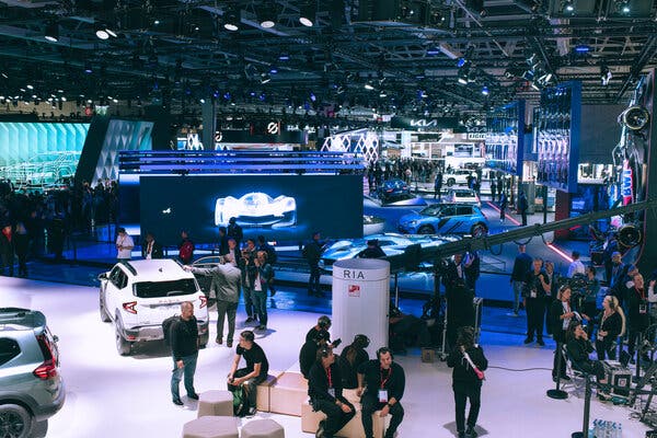 A group of people are sitting and standing around cars on the floor of a large exhibition space.