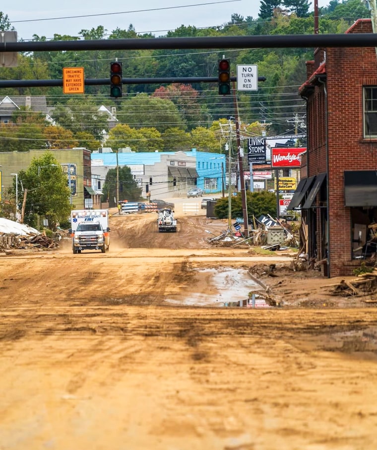 An ambulance drives on a dirt road between buildings