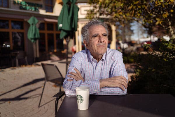 Greg Tutunjian, resting his crossed arms on a table outside with a Starbucks coffee cup in front of him.