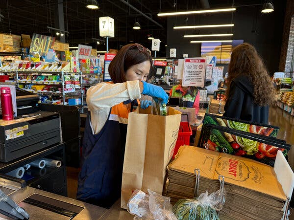 A woman packs groceries into a brown paper bag at a supermarket.