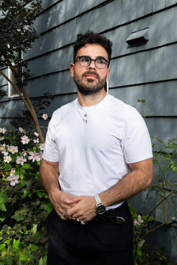 Hen Mazzig standing in front of a flowering plant outside a gray house.