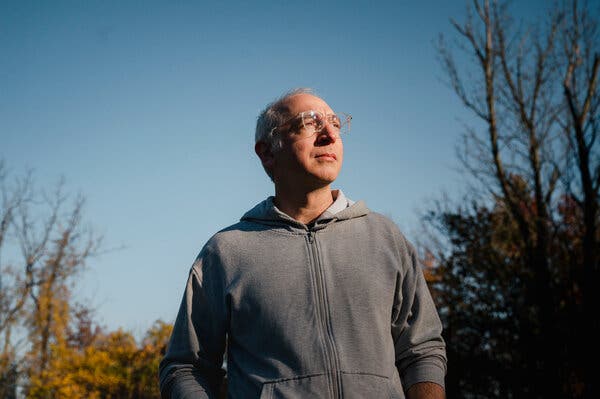 Chris Mancinelli stands outside, wearing a zipped-up gray sweatshirt with the hood down.