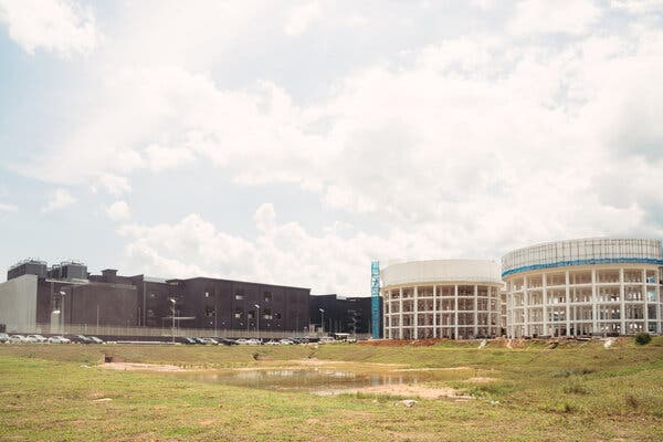 The white skeleton of two round buildings under construction alongside a two-floor brown building.