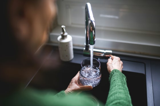 Close up of a senior woman's hand filling a glass of filtered water right from the tap in the kitchen sink at home