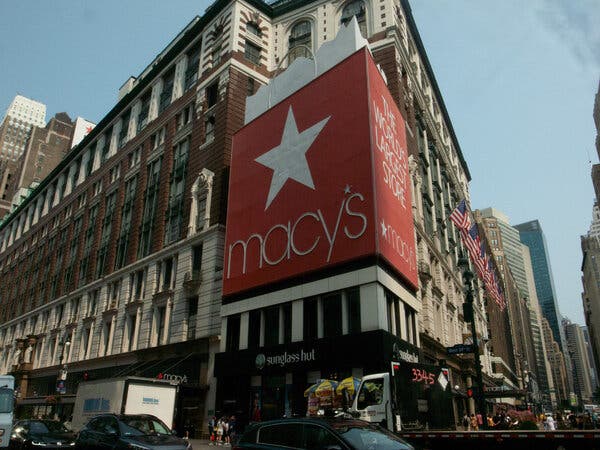 A large Macy’s logo on the side of a building surrounded by traffic on a city street corner.