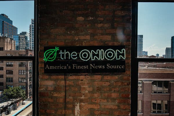 A neon sign that has a green logo of an onion hangs on a brick wall surrounded by windows overlooking a cityscape.