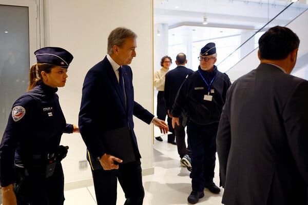 Bernard Arnault, in a dark suit, surrounded by security personnel.