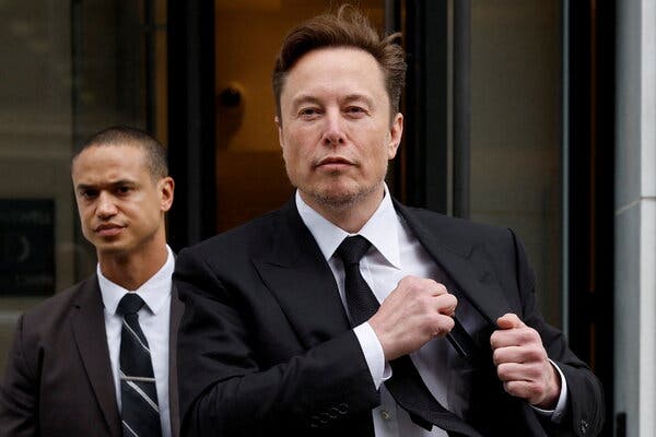 Elon Musk reaches into a pocket of his black suit jacket while walking outside.