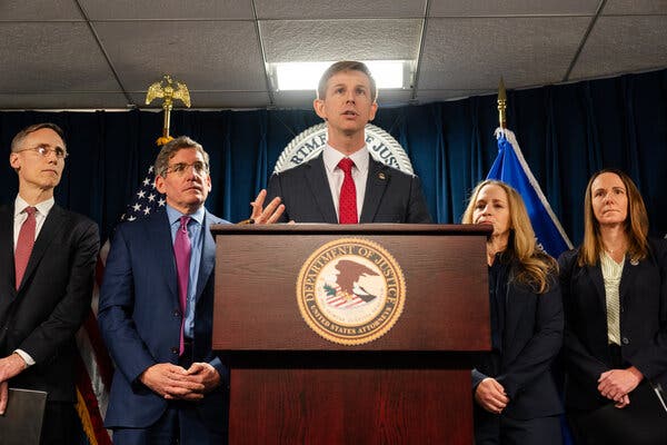 A man in a suit speaking into a lectern, surrounded by colleagues.