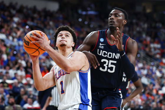 250323-huskies-gators-vl-211p-2399d1-1 Walter Clayton Jr., left, is holding a basketball aiming for the basket and is guarded by Samson Johnson on the basketball court